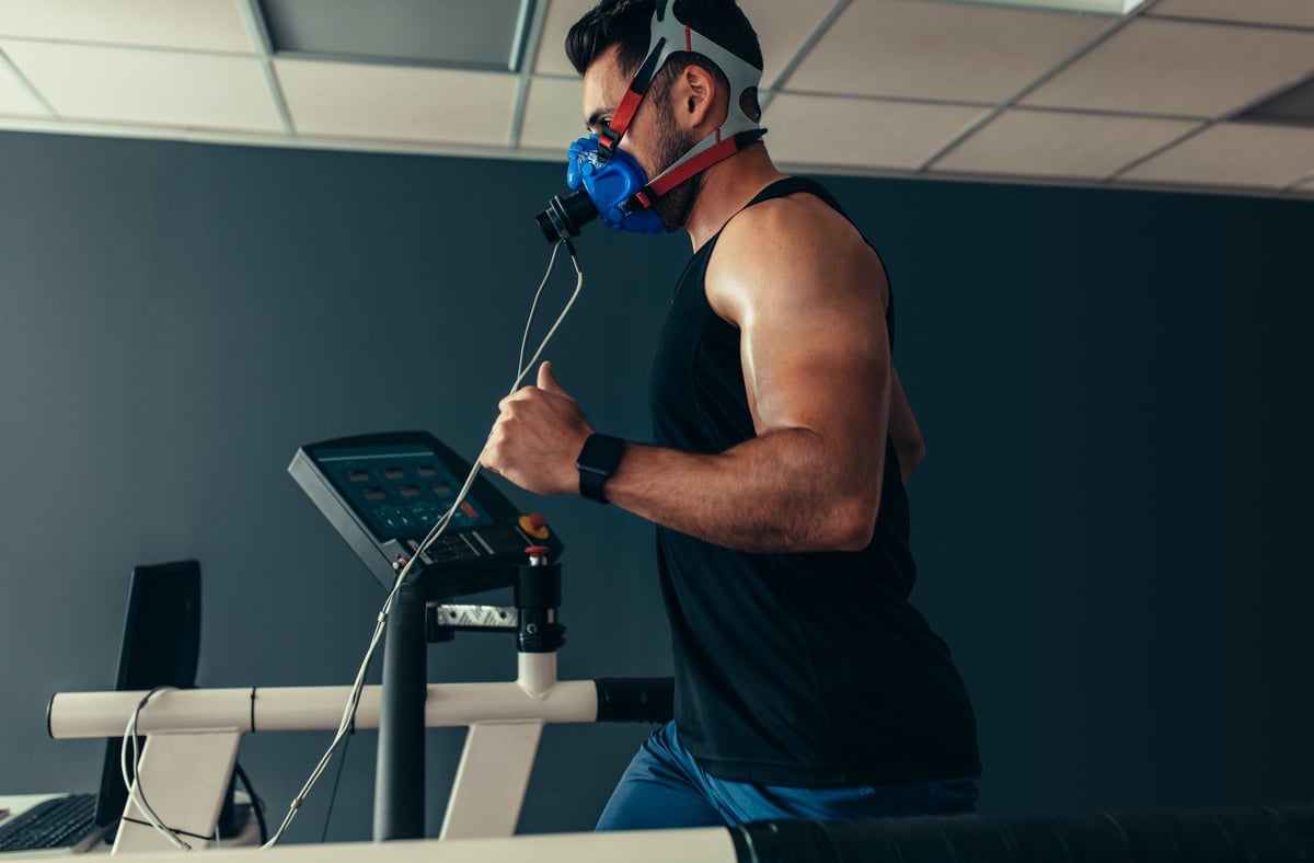 Male athlete wearing an oxygen mask while running on a treadmill in a sports science lab